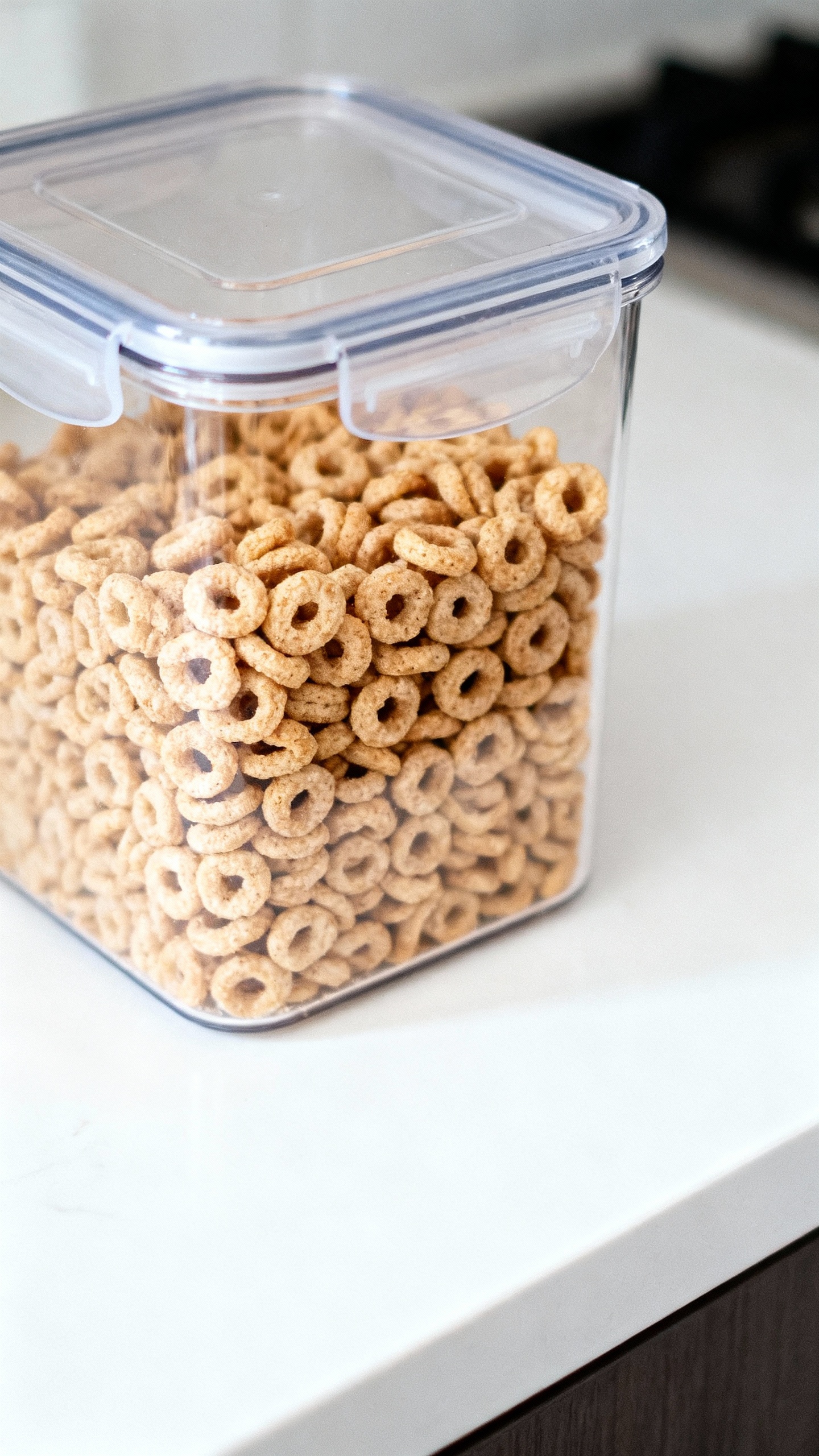 Closeup of clear airtight cereal container, crunchy loops, white countertop
